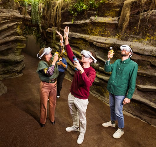 Two children in MR headsets holding yellow explorer tools in front of a fossil wall